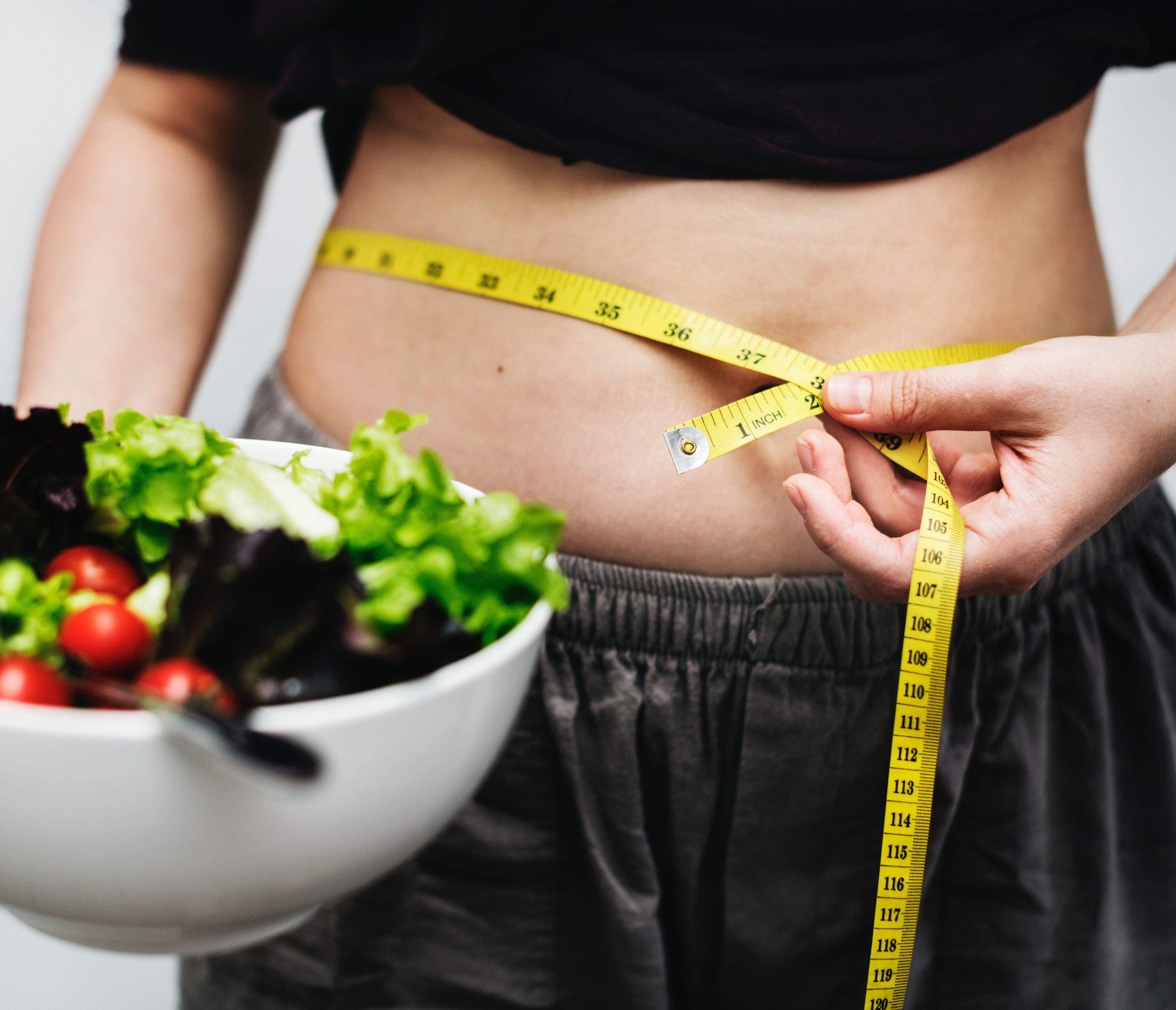 a slim lady measuring waist, holding a salad