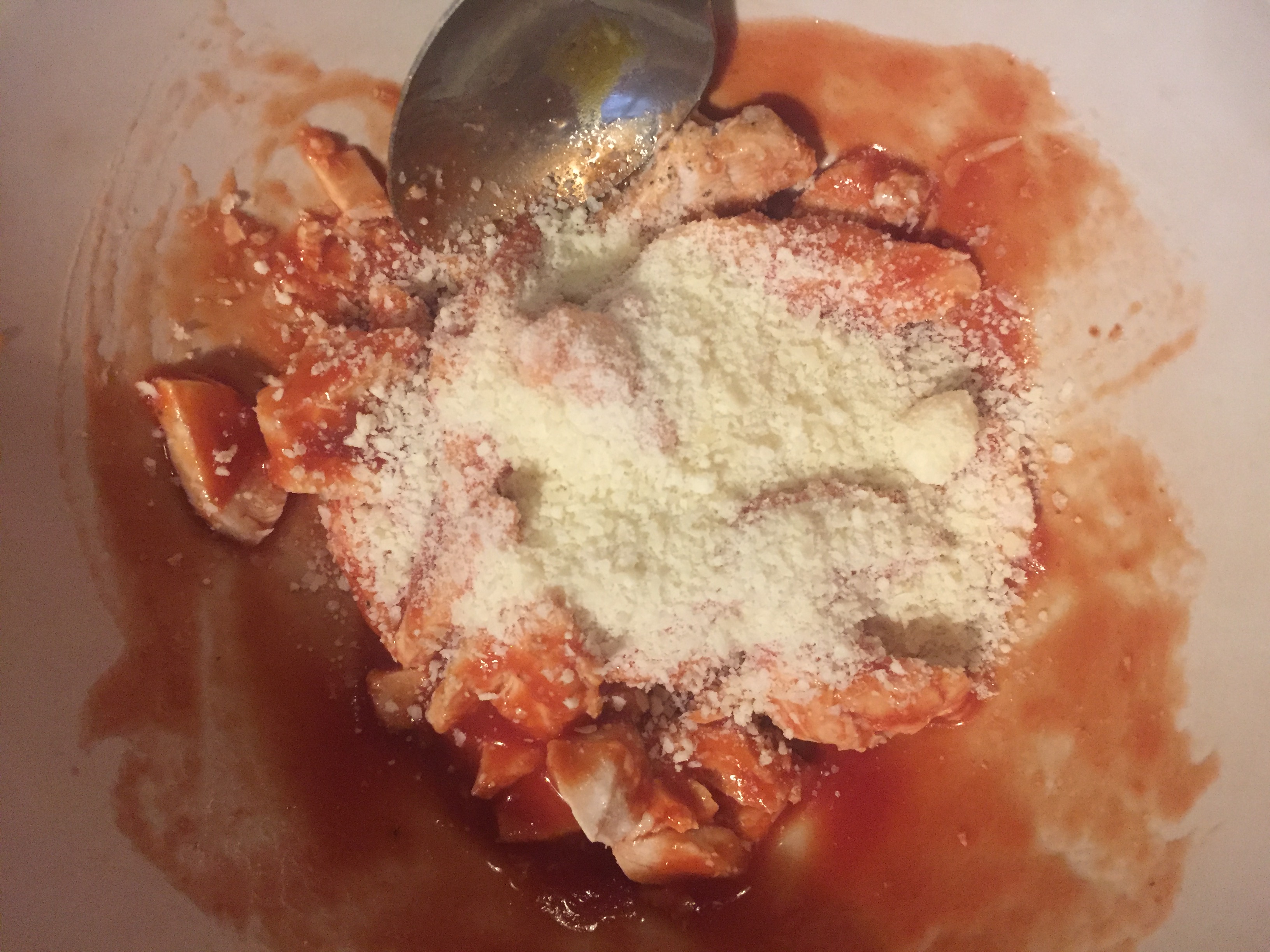 Chicken pieces with tomato and parmesan mixed together in a bowl